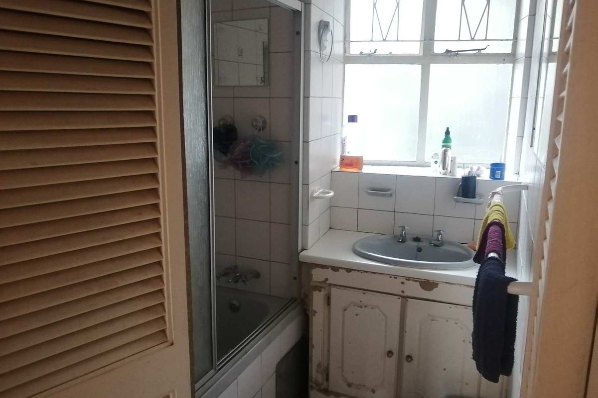 A dated bathroom featuring a built-in vanity cabinet, tiled walls, and a shower-over-bath combination with a sliding glass screen.