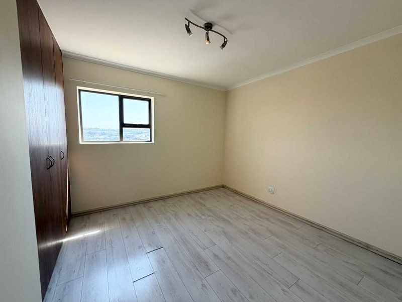 An empty bedroom featuring light-toned laminate flooring, built-in wooden cupboards, and a ceiling-mounted light fixture.
