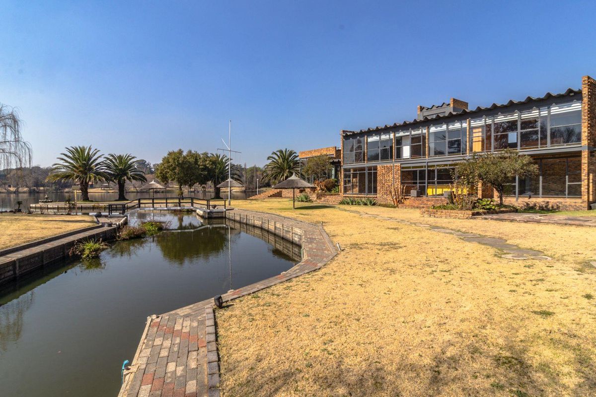 Spacious rear exterior view featuring a large brick residence with extensive glass windows, overlooking a private canal and landscaped garden area.