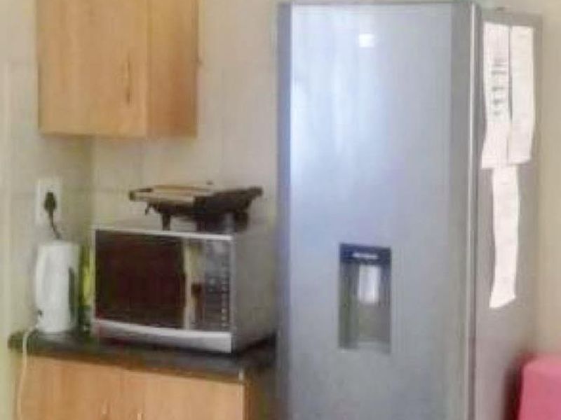 A compact kitchen area featuring laminate cabinetry, dark countertops, and a tiled splashback, providing functional storage and workspace.