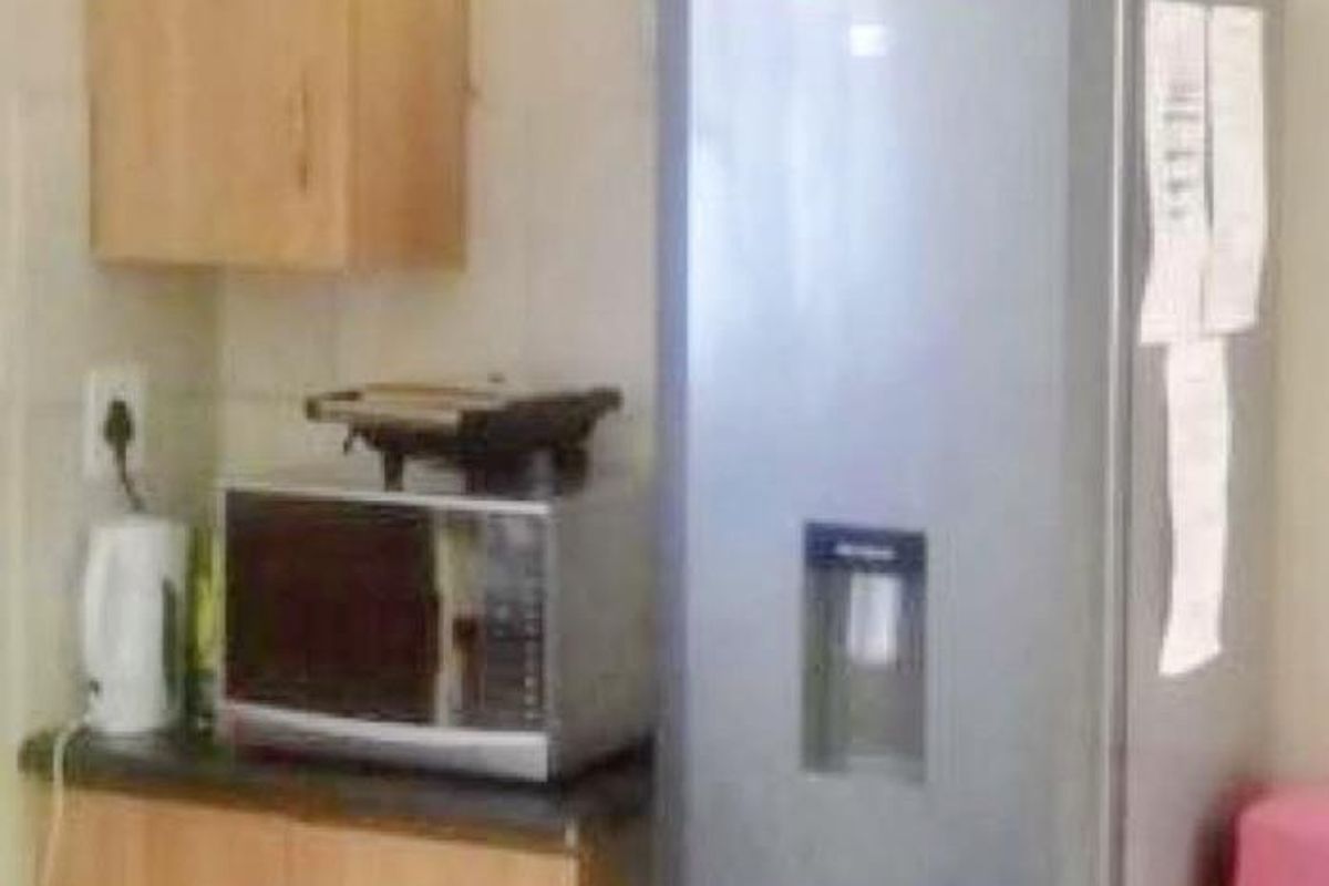 A compact kitchen area featuring laminate cabinetry, dark countertops, and a tiled splashback, providing functional storage and workspace.