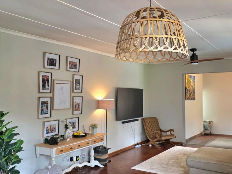 A comfortable living room featuring hardwood flooring, a ceiling fan, and decorative cove cornicing, creating a warm and inviting atmosphere.