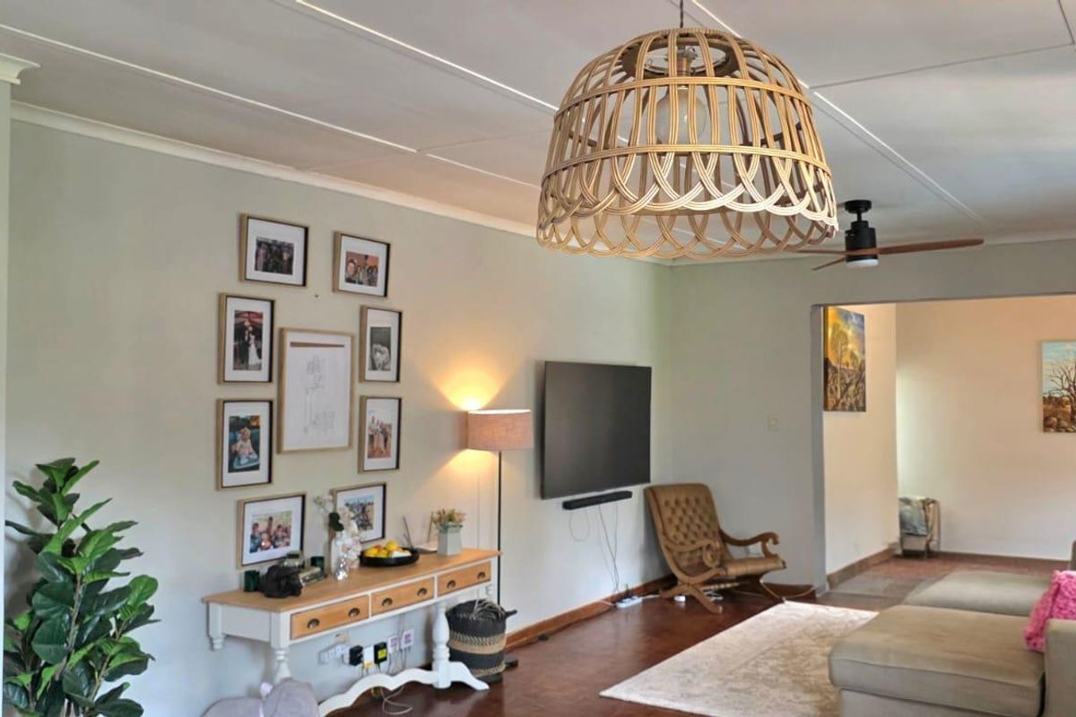 A comfortable living room featuring hardwood flooring, a ceiling fan, and decorative cove cornicing, creating a warm and inviting atmosphere.