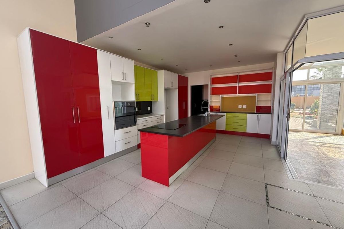 Modern kitchen featuring a central island, high-gloss red and lime cabinetry, built-in oven, and large format floor tiles with direct patio access.