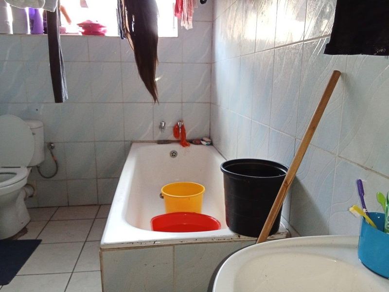 A functional bathroom featuring a standard bathtub, toilet, and tiled surfaces, currently requiring maintenance and cosmetic updates to improve its overall condition.