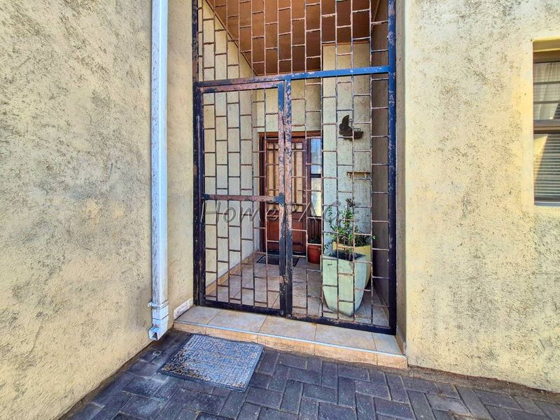 Entrance area featuring a security gate, tiled flooring, and textured exterior walls.