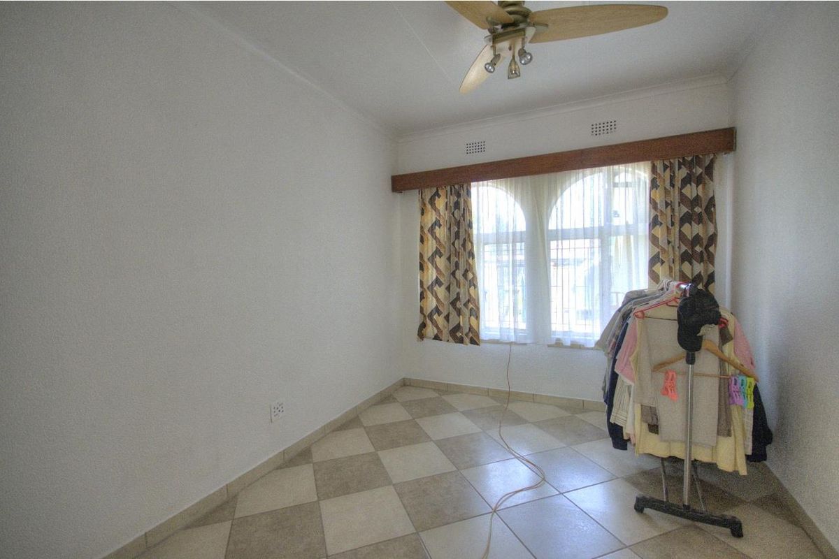 A bedroom featuring tiled flooring, a ceiling fan, and arched windows with decorative pelmet detailing.