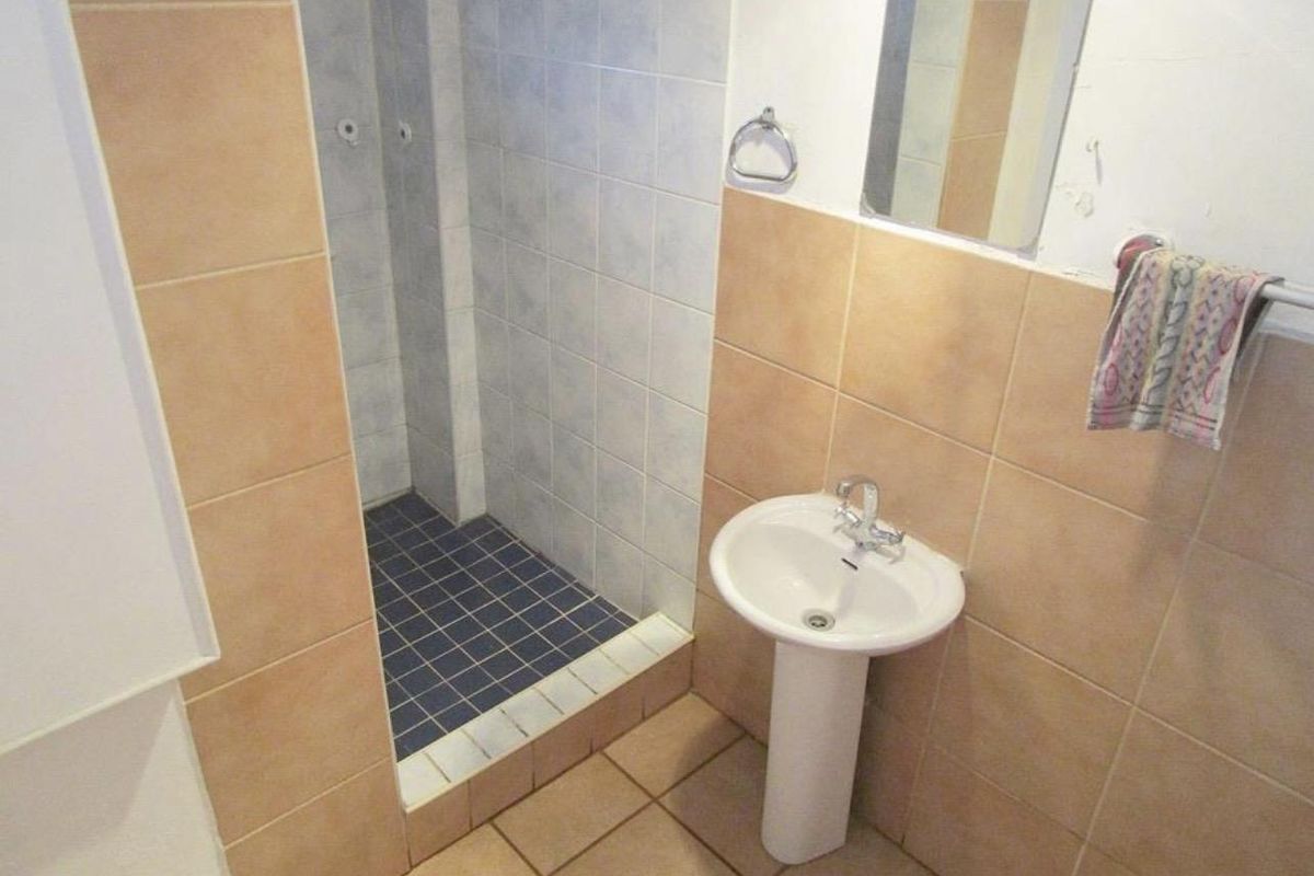A functional bathroom featuring a pedestal sink, a tiled shower enclosure, and neutral wall and floor tiling.