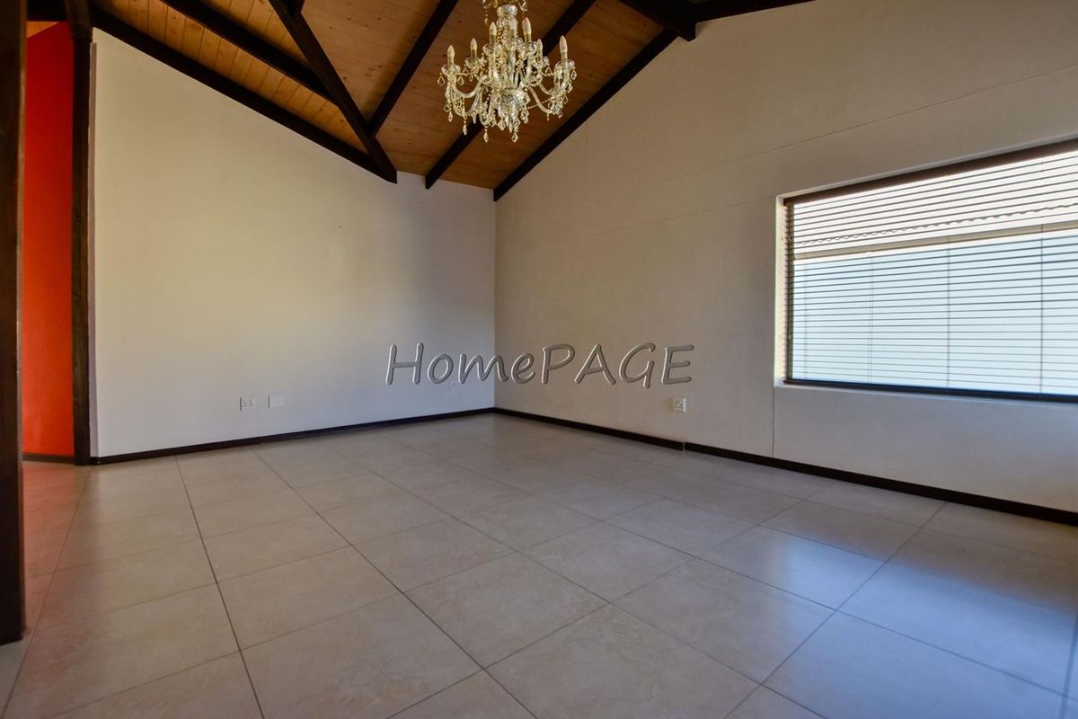 Spacious living area featuring high vaulted timber ceilings, exposed beams, tiled flooring, and a large window with fitted blinds.