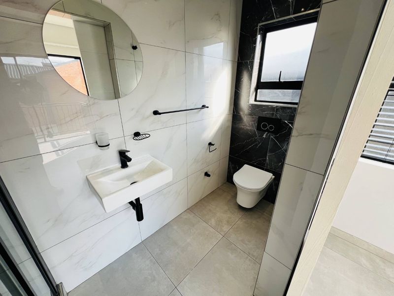 Modern bathroom featuring high-end marble-look wall tiles, a wall-hung toilet with concealed cistern, and sleek black matte fixtures.