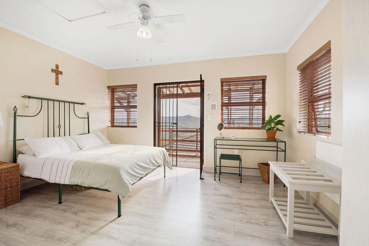 A bright bedroom featuring light wood-look flooring, a ceiling fan, and direct access to an outdoor balcony through a security gate.