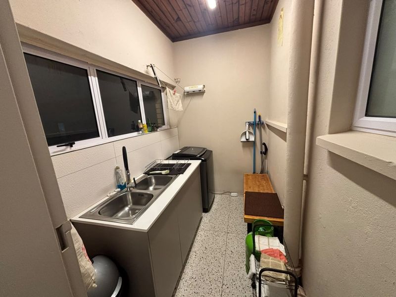 A functional laundry area featuring a double stainless steel sink, built-in cabinetry, terrazzo flooring, and a timber-paneled ceiling.