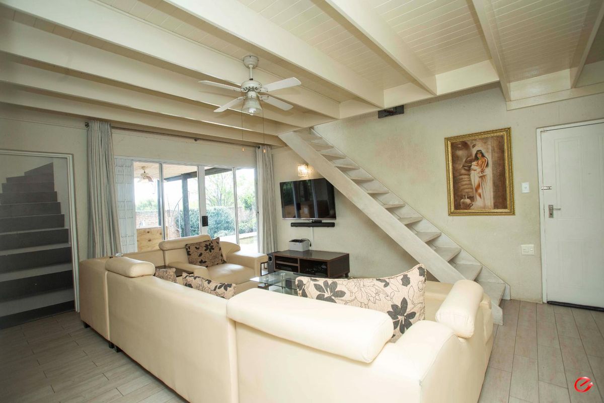 Spacious living area featuring exposed beam ceilings, tiled flooring, and a staircase leading to the upper level, with direct access to the patio.