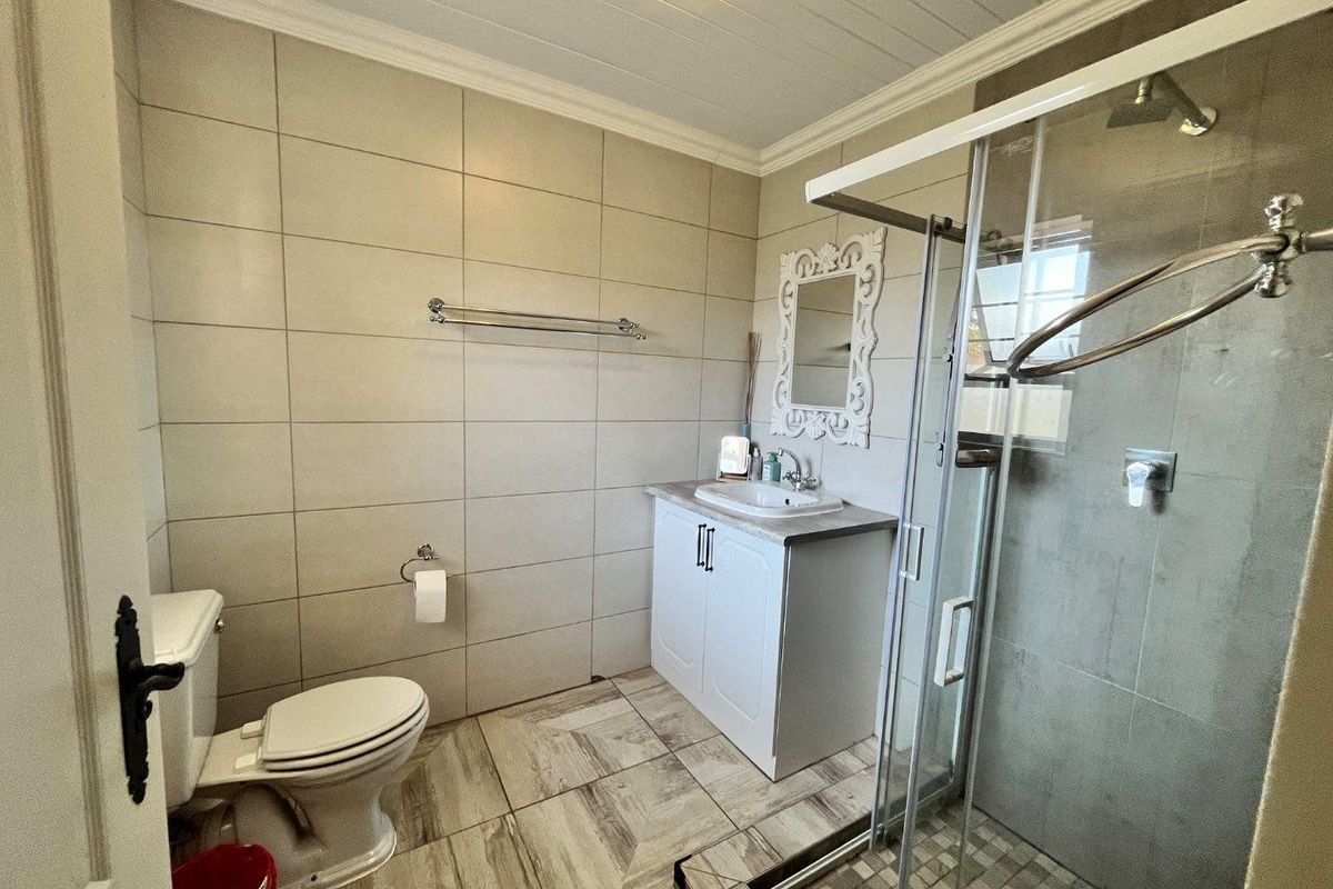 A functional bathroom featuring a glass shower enclosure, vanity cabinet with basin, toilet, and neutral wall and floor tiling.