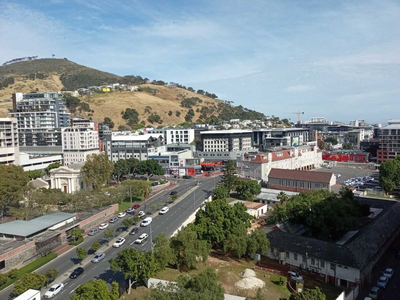An elevated aerial view of the surrounding urban landscape, featuring city streets, commercial buildings, and nearby mountain terrain.