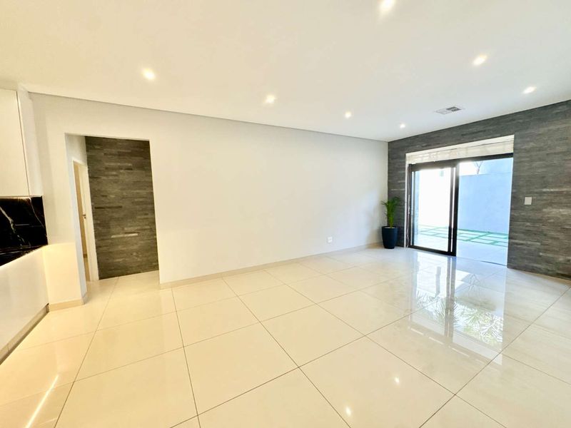 Spacious open-plan living area featuring polished porcelain tiles, recessed lighting, and a modern stone feature wall with direct access to an outdoor patio.