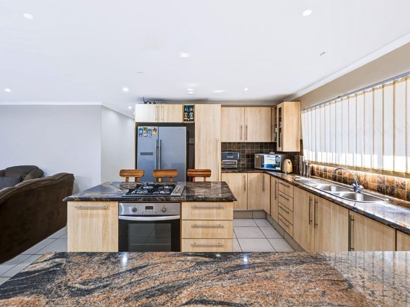 Open-plan kitchen featuring granite countertops, wooden cabinetry, built-in oven, gas hob, and double basin sink, seamlessly integrated with the living area.