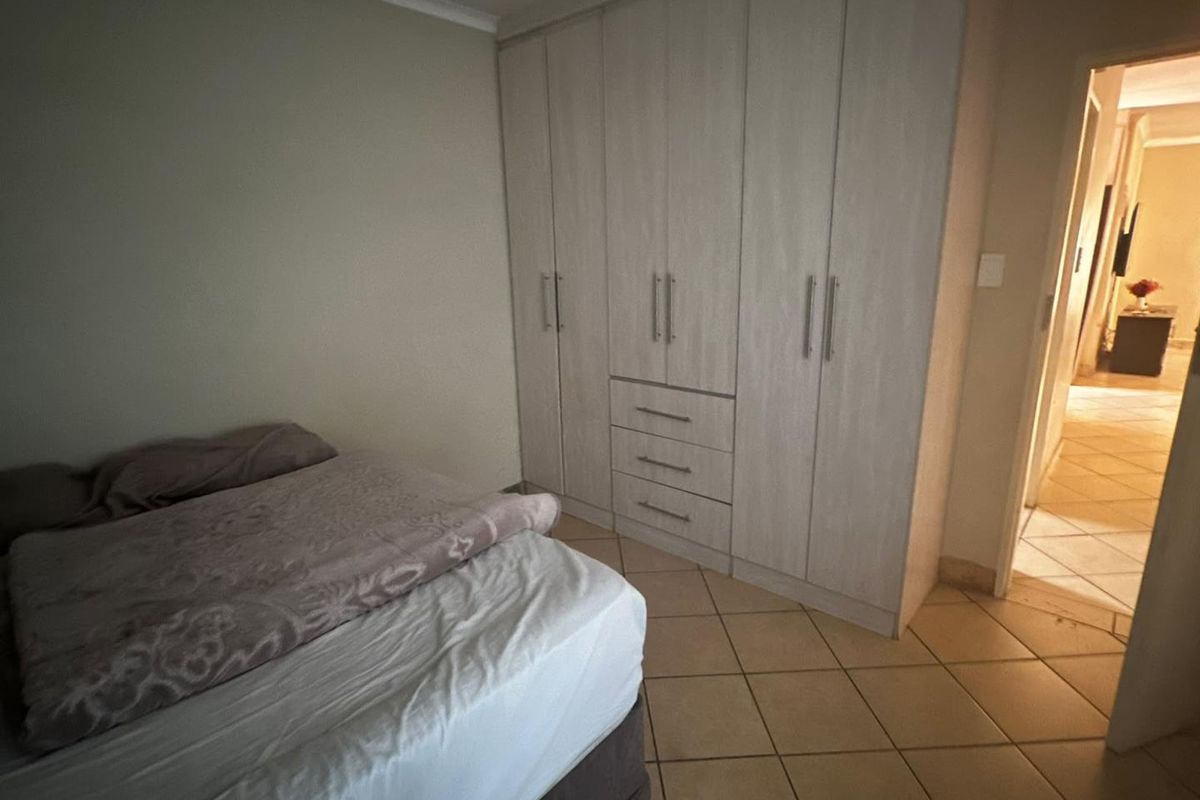 A bedroom featuring built-in cupboards with light wood-grain finish and tiled flooring, providing functional storage space.