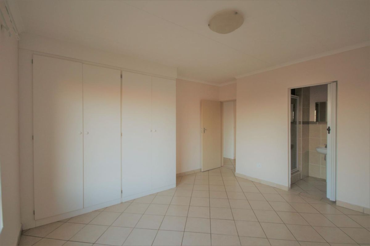 A spacious, empty bedroom featuring neutral tiled flooring, built-in cupboards, and direct access to an en-suite bathroom.