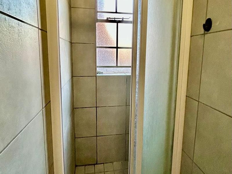 A compact shower cubicle featuring tiled walls, a tiled floor, and an obscured glass window for privacy and natural light.