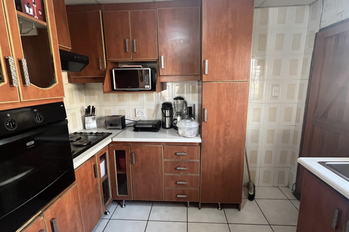 A functional kitchen featuring wood-tone cabinetry, built-in oven, gas hob, and tiled finishes, offering a classic layout with ample storage space.