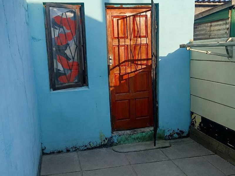 A small rear exterior area featuring a paved patio, a wooden door with a security gate, and a window with security bars.