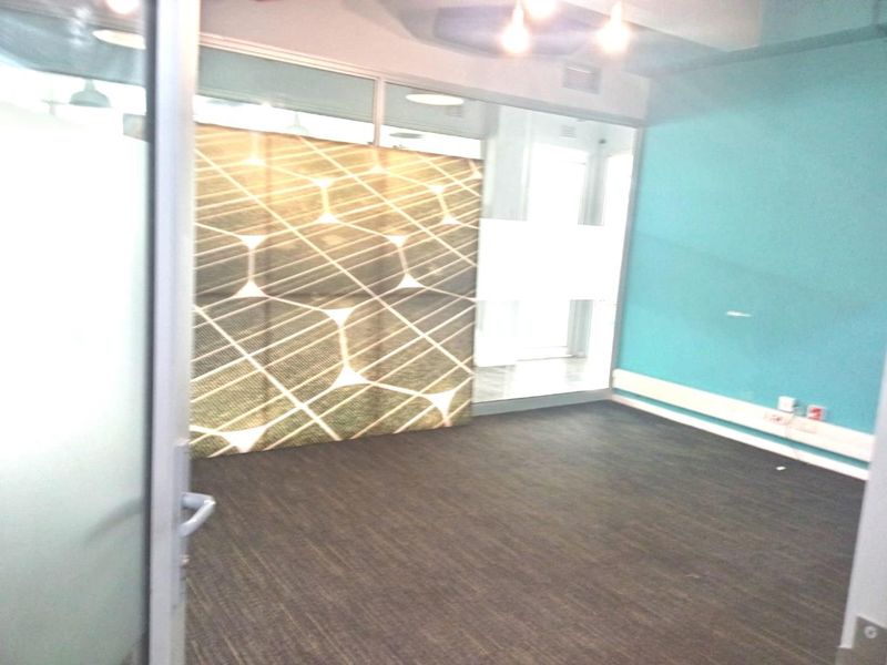 An empty office space featuring glass partitions, dark laminate flooring, and modern recessed lighting, providing a clean and professional environment.
