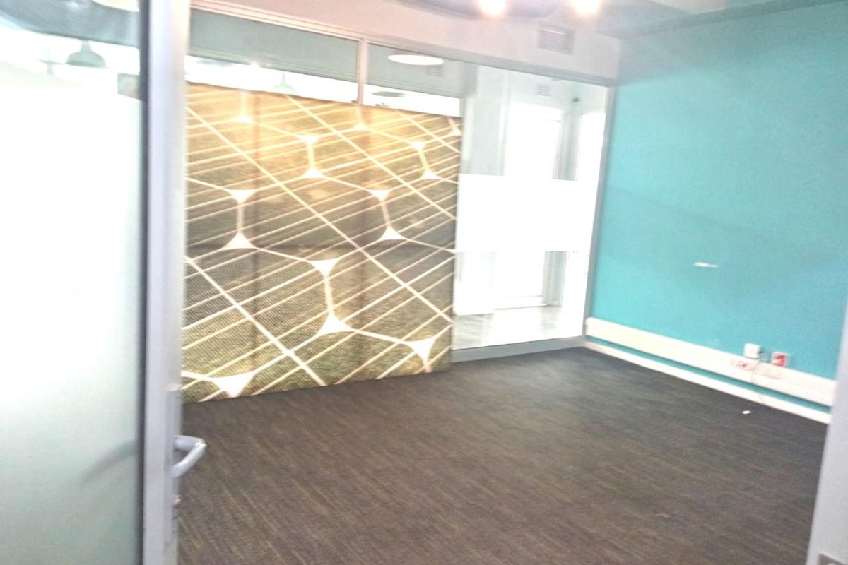 An empty office space featuring glass partitions, dark laminate flooring, and modern recessed lighting, providing a clean and professional environment.
