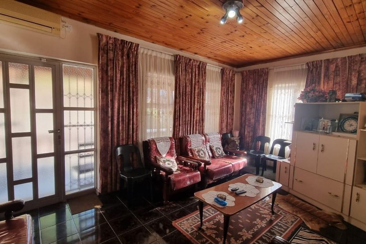 A living room featuring a timber tongue and groove ceiling, tiled flooring, and a glass panelled door with access to the exterior.