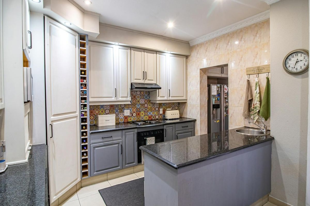 A well-appointed kitchen featuring granite countertops, built-in cabinetry, a decorative tiled backsplash, integrated hob and oven, and a convenient breakfast bar with sink.