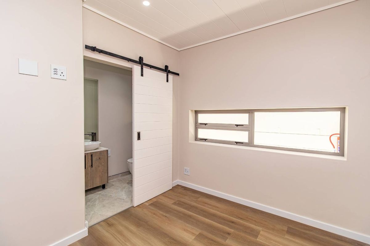 A bright, modern bedroom featuring laminate flooring, a sliding barn door leading to an en-suite bathroom, and a horizontal window for natural light.