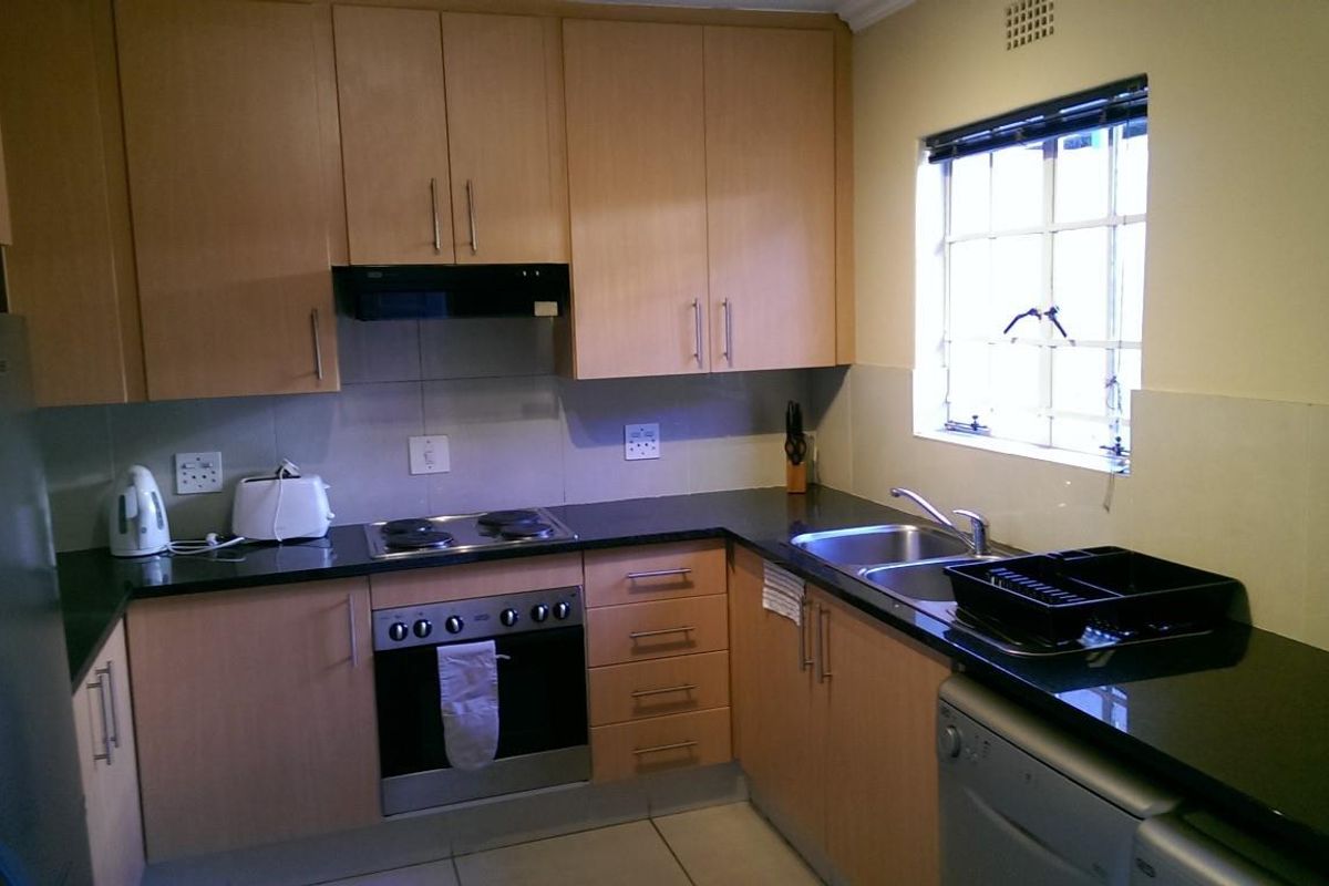 Functional kitchen featuring light wood-finish cabinetry, contrasting black granite countertops, built-in oven, electric hob, and a double bowl sink with tiled splashbacks.
