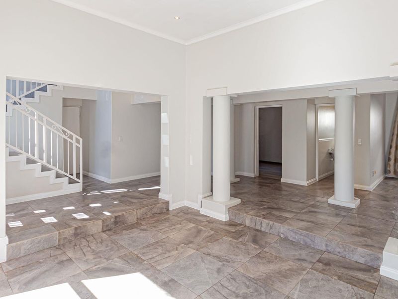Spacious open-plan living area featuring large format floor tiles, structural columns, and a prominent staircase with a decorative metal balustrade.