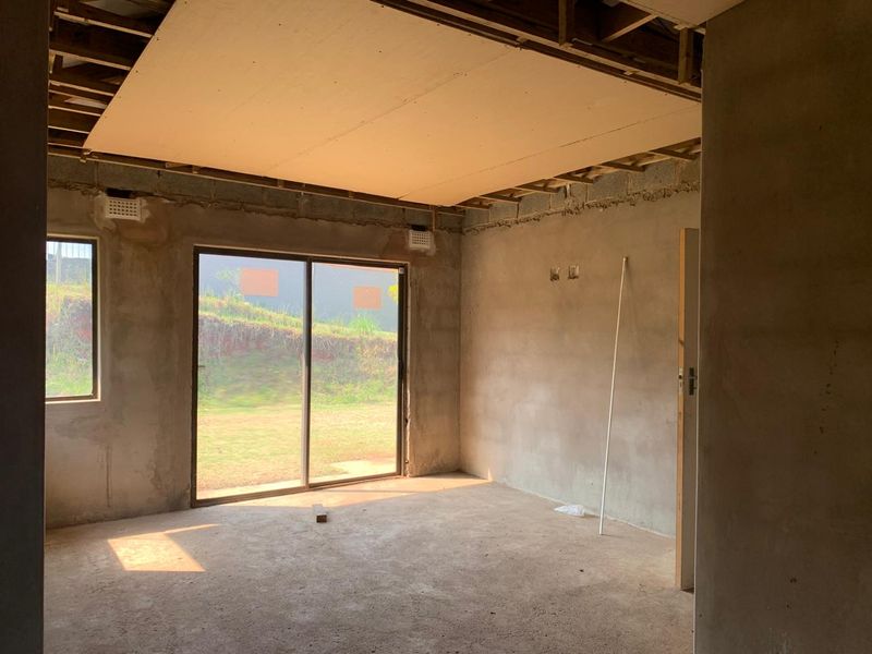 An unfinished living room space featuring exposed concrete block walls, an incomplete ceiling, and a sliding glass door leading to the exterior.