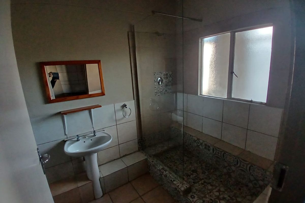 A functional bathroom featuring a pedestal basin, a walk-in shower with decorative patterned tiling, and a frosted glass window for natural light.
