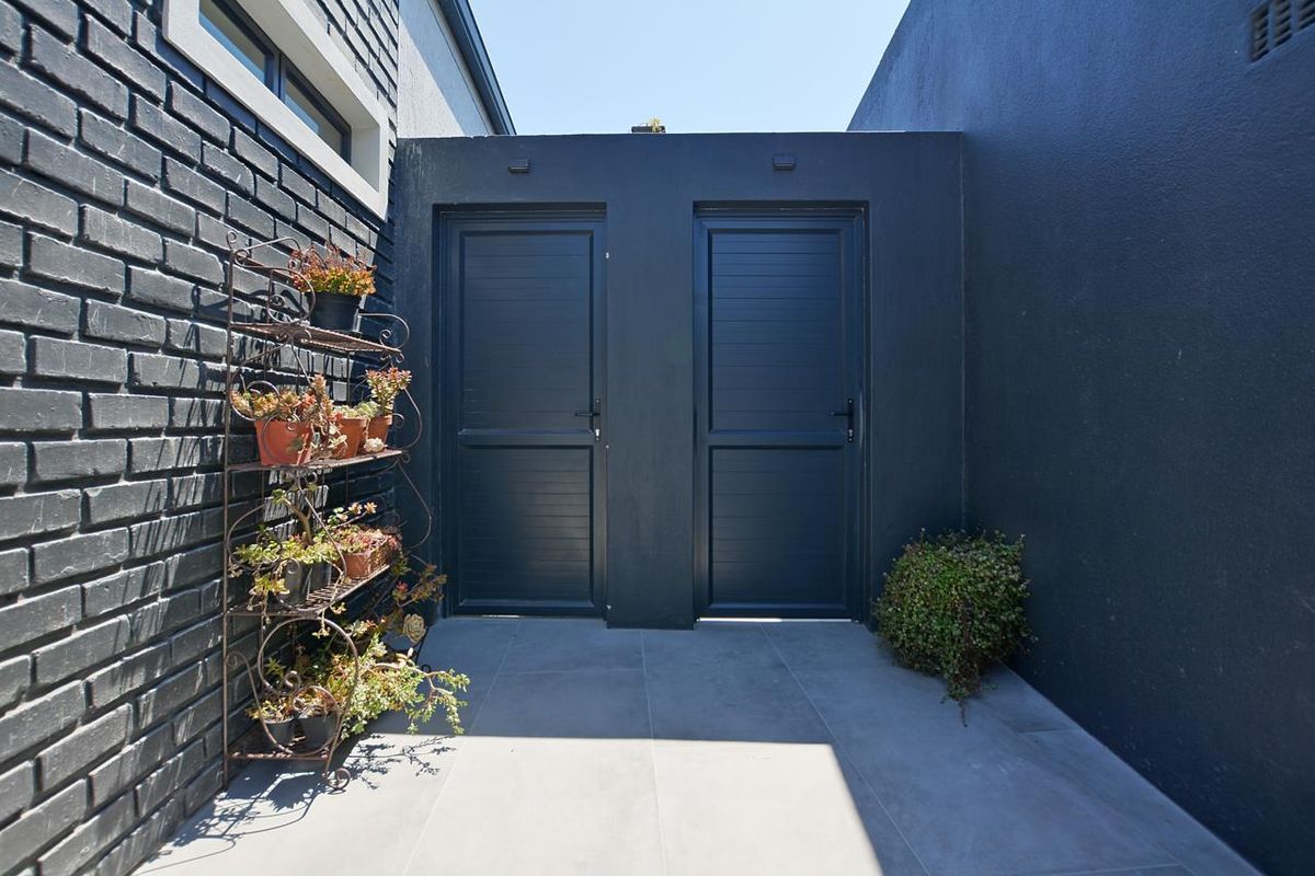 A clean, modern rear exterior courtyard featuring dark painted brick walls, grey tiled flooring, and two secure exterior access doors.