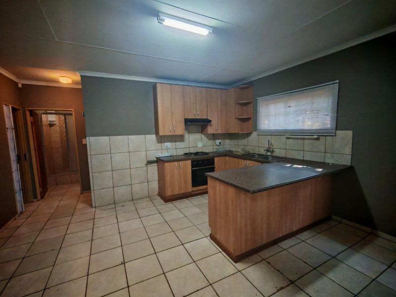 A functional kitchen featuring light wood cabinetry, dark laminate countertops, built-in oven with gas hob, and tiled flooring, offering a practical layout for renovation.
