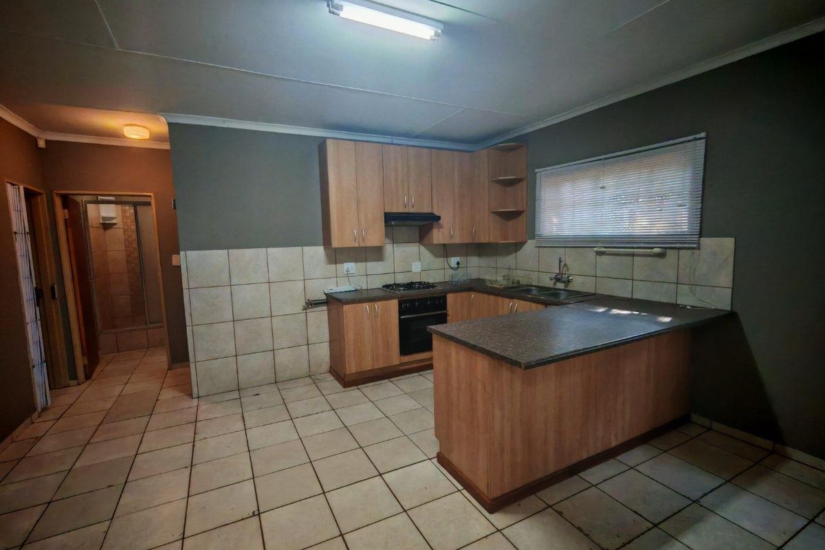 A functional kitchen featuring light wood cabinetry, dark laminate countertops, built-in oven with gas hob, and tiled flooring, offering a practical layout for renovation.