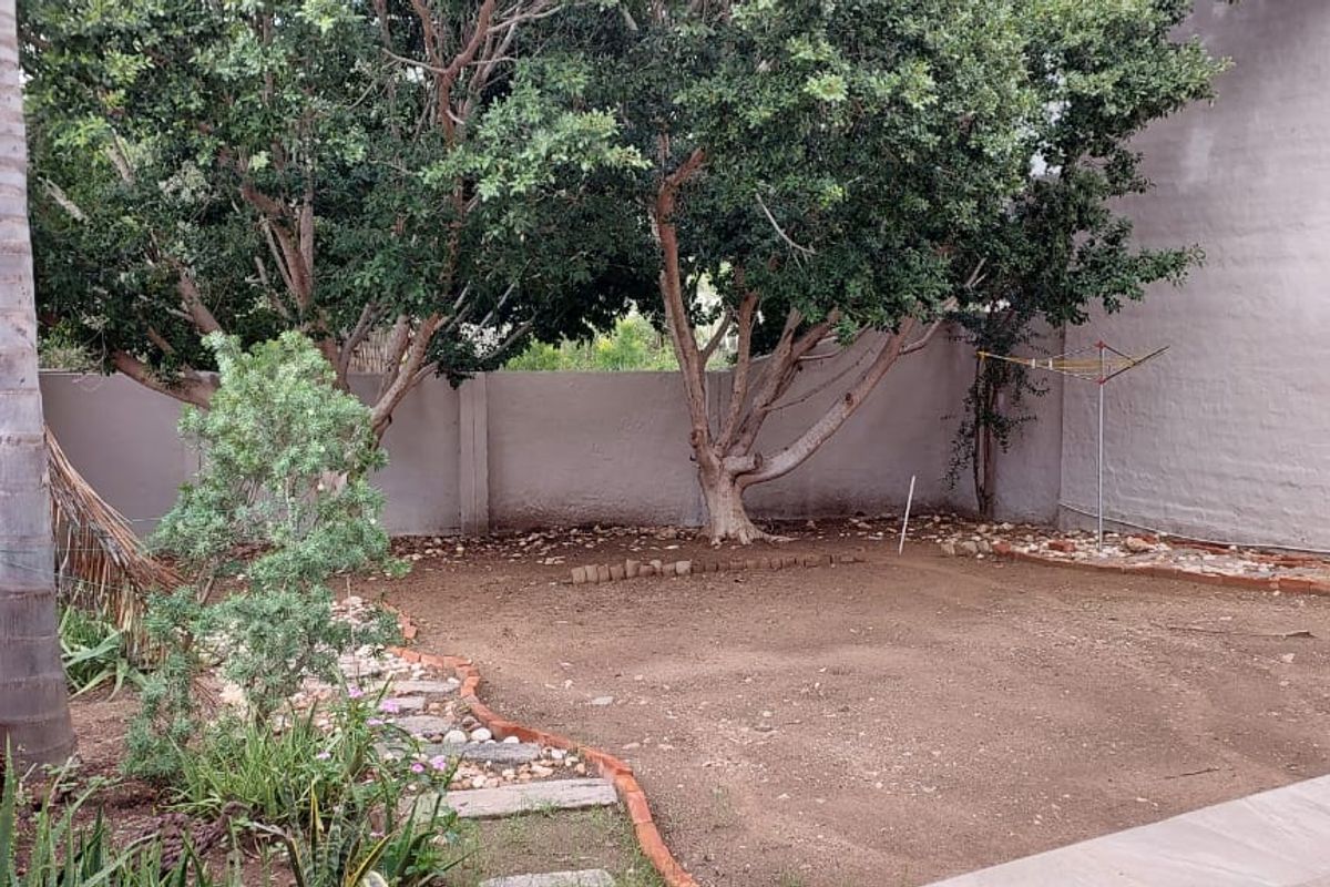 A private rear garden area featuring mature trees, a paved patio edge, and a perimeter boundary wall.