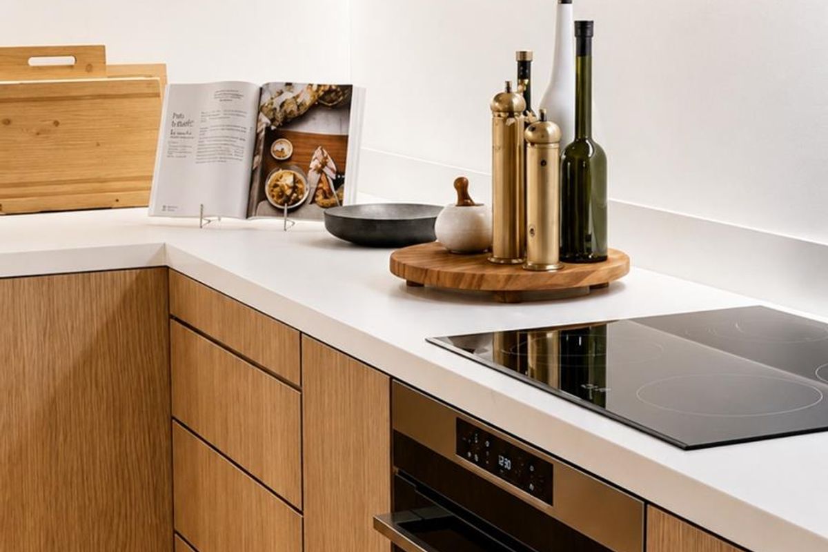 Modern kitchen featuring light oak cabinetry, sleek white countertops, and integrated induction cooktop with built-in oven.