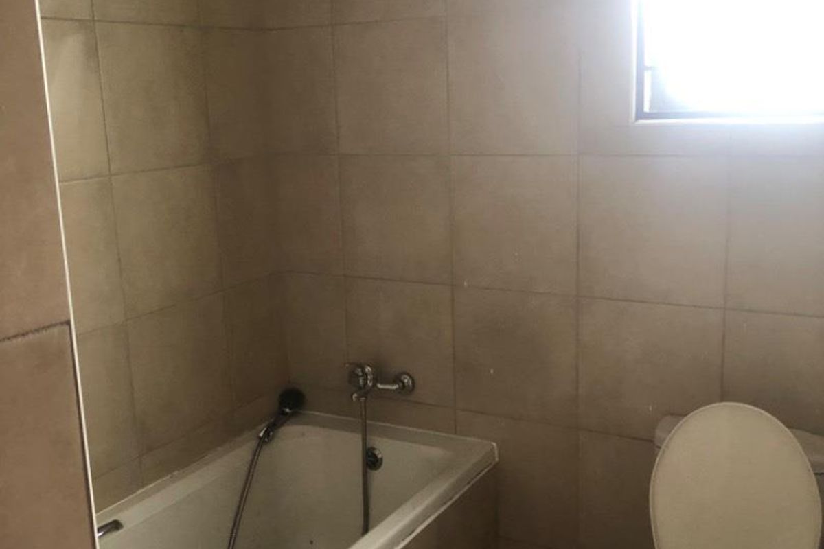 A compact bathroom featuring a built-in bathtub with shower mixer and a standard toilet, finished with neutral wall tiles.