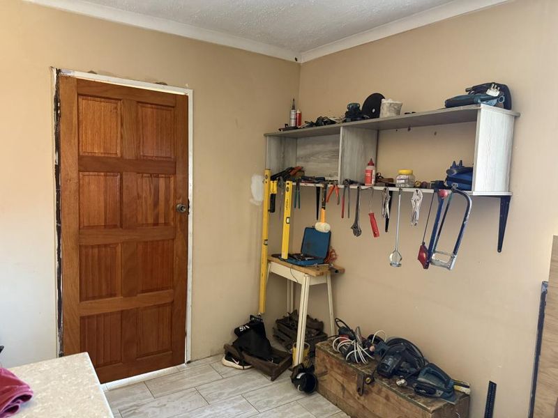 A utility space featuring tiled flooring, a timber door, and wall-mounted shelving, currently used as a workshop area.