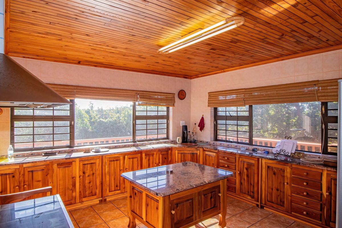 Spacious kitchen featuring timber cabinetry, granite countertops, a central island, and a distinctive timber-clad ceiling with large windows providing natural light.