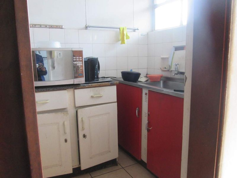 A compact, dated kitchen featuring basic cabinetry, a stainless steel sink, and tiled backsplash, offering potential for a modern renovation.