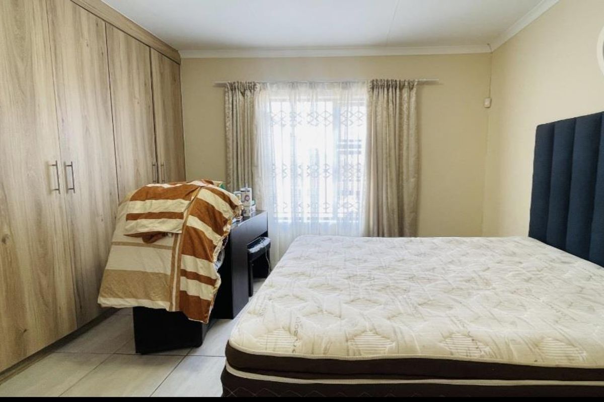 A bedroom featuring built-in wooden cupboards, tiled flooring, and a window with curtaining.