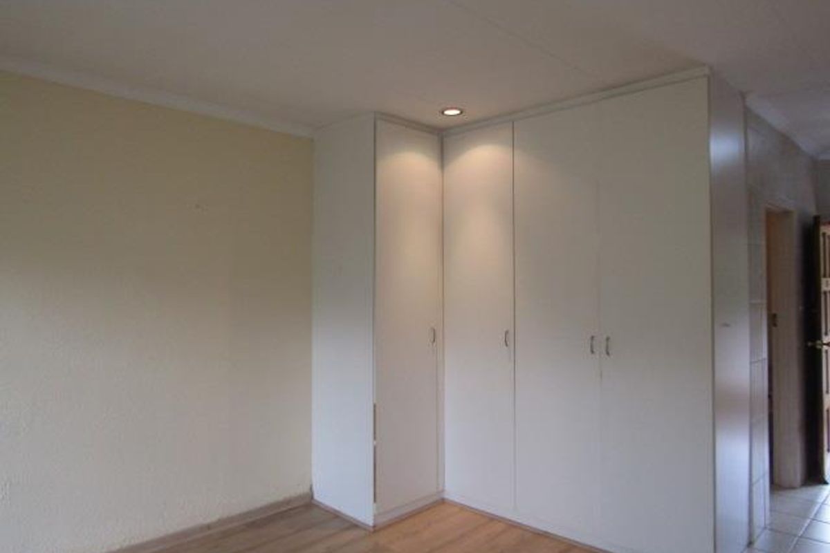 A bedroom featuring built-in white corner cupboards with integrated downlighting and light wood-look flooring.