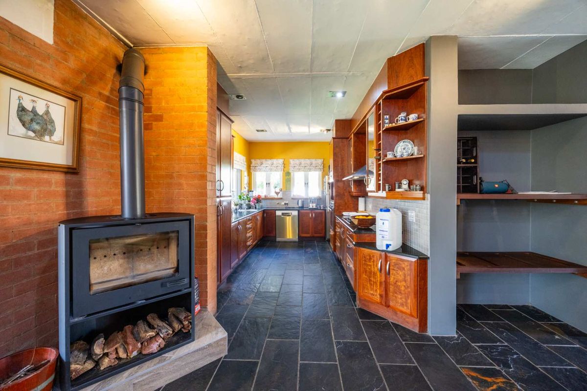 Spacious kitchen featuring slate flooring, extensive wooden cabinetry, stone countertops, and a prominent brick-surround wood-burning fireplace.