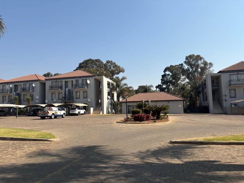 Exterior view of a multi-story apartment complex featuring paved parking areas, covered bays, and well-maintained building facades with balconies.