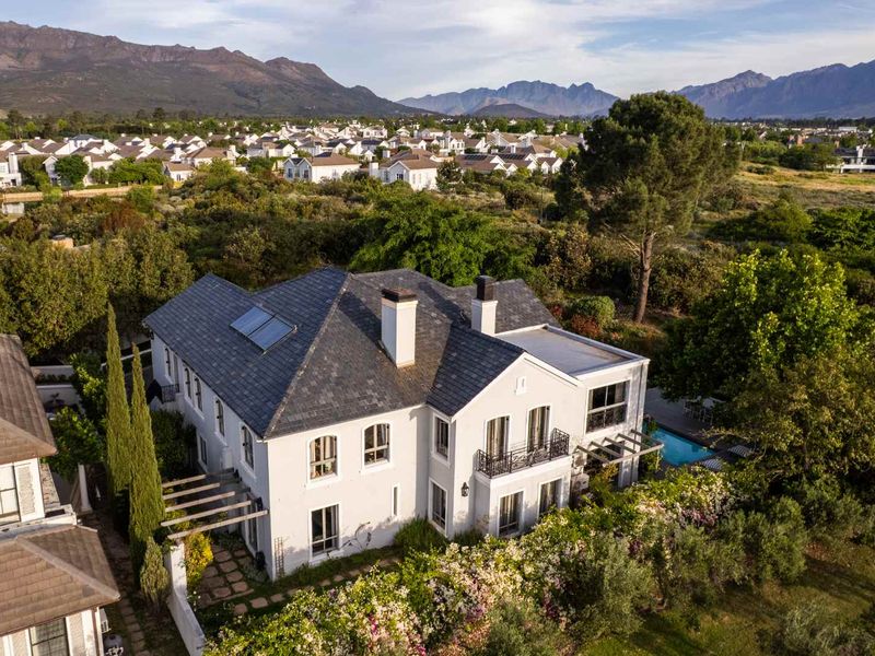 Aerial view of a luxury residence featuring a slate roof, solar panels, swimming pool, and landscaped gardens set against a scenic mountain backdrop.