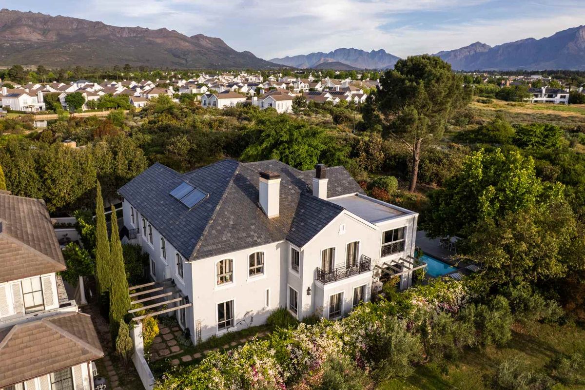 Aerial view of a luxury residence featuring a slate roof, solar panels, swimming pool, and landscaped gardens set against a scenic mountain backdrop.